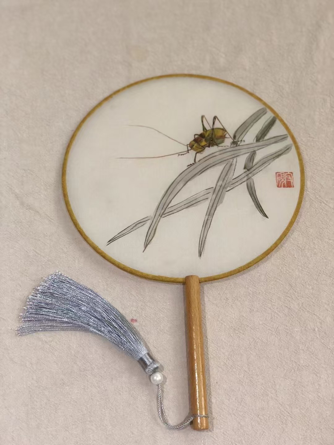 Ink painting on a round fan: grasses and a katydid