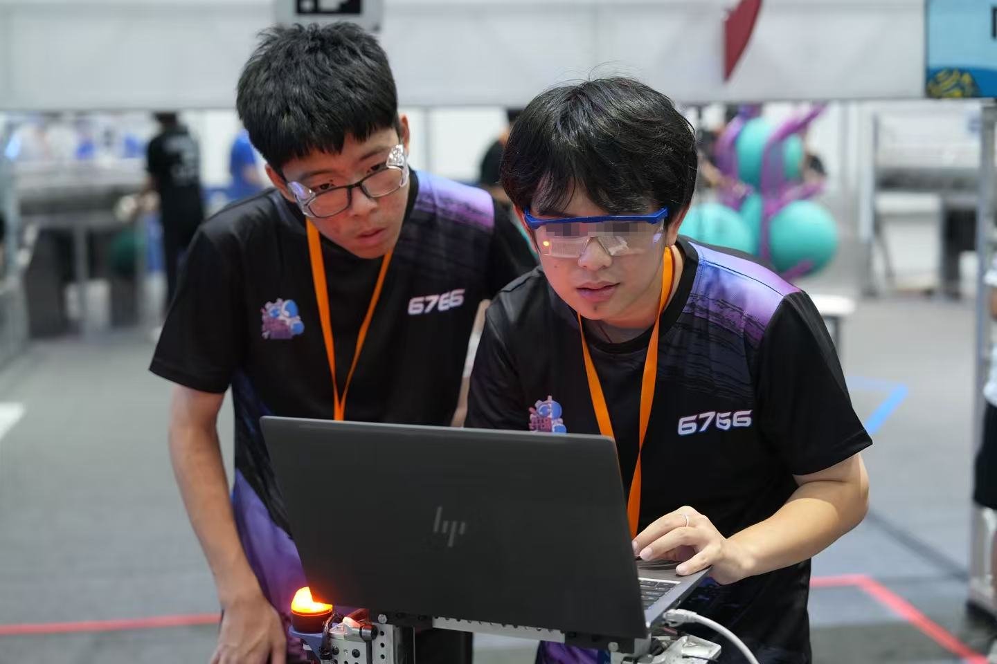 Testing code with a teammate on a laptop beside the practice field